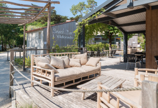 Outdoor lounge at Camping Les Cyprès - Glampingtenten Vendée, with wooden furniture and sunny terrace.