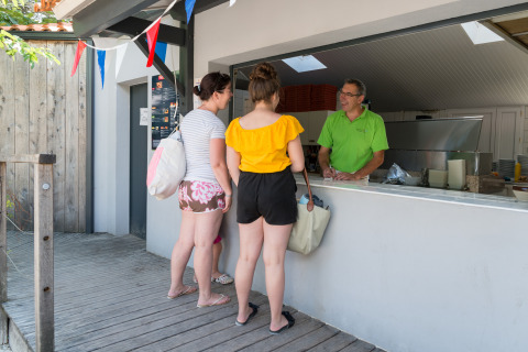 Dos mujeres hacen un pedido en un puesto exterior en Camping Les Cyprès - Glampingtenten Vendée con banderines.