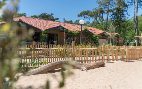 Alojamiento glamping en Camping Les Cyprès, Vendée, con valla de madera, área de arena y vegetación.