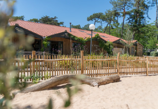 Glamping-Unterkunft Camping Les Cyprès in Vendée mit Holzzaun, Sand und Bäumen bei sonnigem Wetter.