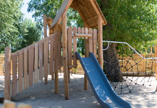 Parque infantil de madera con tobogán y red de escalar en Camping Les Cyprès - Glampingtenten Vendée bajo los árboles.