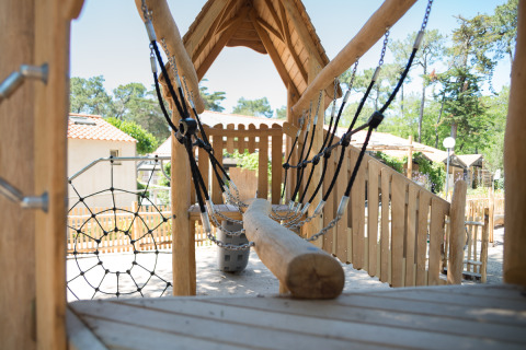 Área de juegos con puente de madera y red en Camping Les Cyprès - Glampingtenten Vendée rodeado de naturaleza.