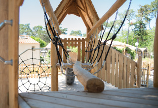 Playground with wooden bridge and climbing net at Camping Les Cyprès - Glampingtenten Vendée surrounded by nature.