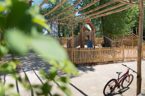 Legeplads med træhegn og legeredskaber på Camping Les Cyprès - Glampingtenten Vendée i solskin.