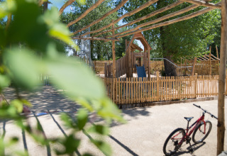 Legeplads med træhegn og legeredskaber på Camping Les Cyprès - Glampingtenten Vendée i solskin.
