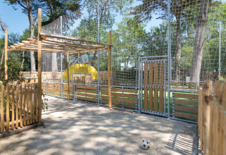 Outdoor play area with fenced sports field and basketball hoop at Camping Les Cyprès - Glampingtenten Vendée.