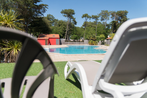 Solrige liggestole ved poolen på Camping Les Cyprès - Glampingtenten Vendée omgivet af grøn natur.