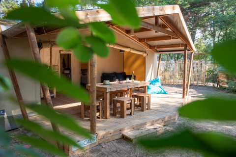 Hébergement glamping avec terrasse en bois, table et bancs au Camping Les Cyprès en Vendée, entouré de verdure.