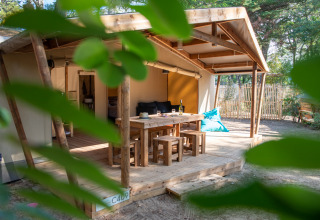 Glampingverblijf met houten terras, tafel en banken bij Camping Les Cyprès in Vendée, omringd door groen.
