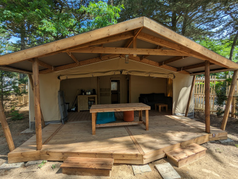 Alojamiento glamping en Camping Les Cyprès, Vendée: tienda espaciosa con terraza de madera rodeada de naturaleza.