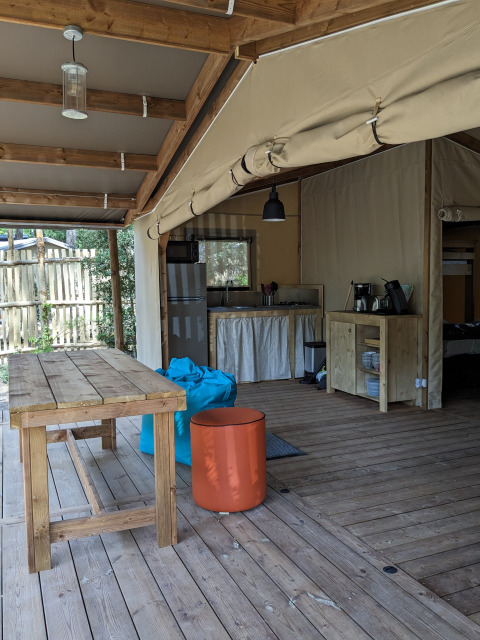 Hébergement glamping en extérieur avec table en bois et coin cuisine au Camping Les Cyprès, Vendée.