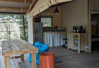 Buiten glamping accommodatie met houten tafel, keuken en zitruimte bij Camping Les Cyprès - Vendée.