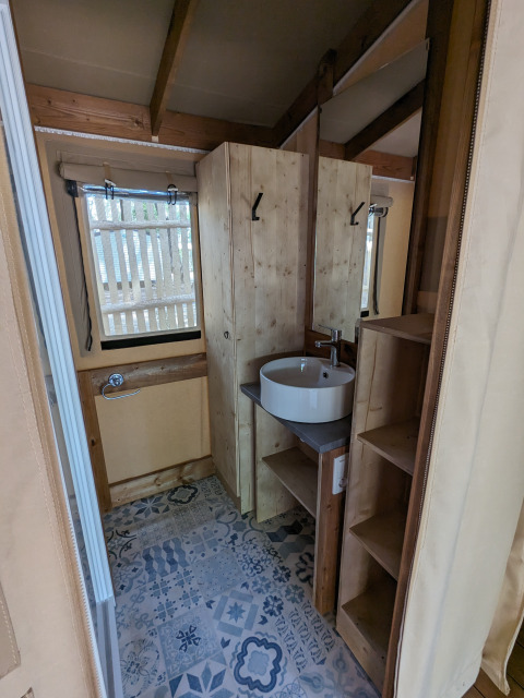 Baño en tienda glamping de Camping Les Cyprès - Glampingtenten Vendée, con paredes de madera y lavabo moderno.