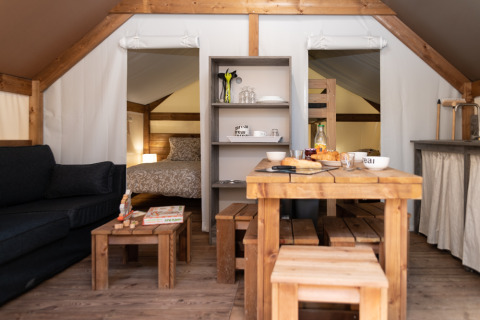 Innenansicht eines Glampingzelts bei Camping Les Cyprès mit Holzmöbeln, Bett und Sofa.