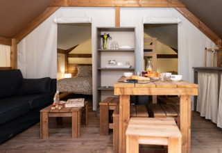 Innenansicht eines Glampingzelts bei Camping Les Cyprès mit Holzmöbeln, Bett und Sofa.
