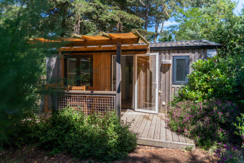 Cabane en bois avec terrasse entourée de verdure au Camping Les Cyprès - Glampingtenten Vendée en France.