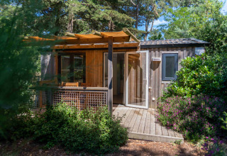 Træhytte med terrasse omgivet af frodig natur ved Camping Les Cyprès - Glampingtenten Vendée i Frankrig.