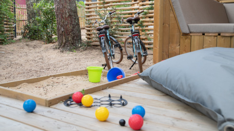 Vista de la terraza de una tienda glamping con arenero, juguetes y bicicletas en Camping Les Cyprès.