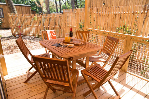 Table et six chaises en bois sur la terrasse d’une tente glamping au Camping Les Cyprès en Vendée, France.