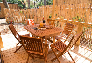 Holztisch und sechs Stühle auf Terrasse im Glamping Les Cyprès in Vendée, eingerahmt von Holzzaun.