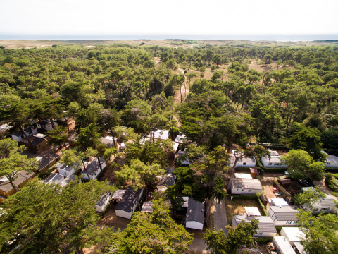 Luchtfoto van Camping Les Cyprès - Glampingtenten Vendée met chalets en veel bomen vlakbij de kustlijn.