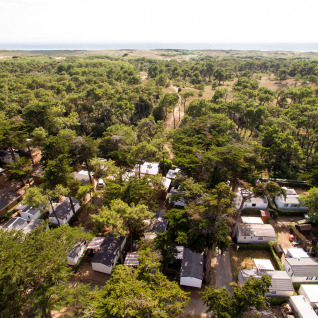 Vista aerea di Camping Les Cyprès - Glampingtenten Vendée con case mobili immerse tra alberi vicino alla costa.
