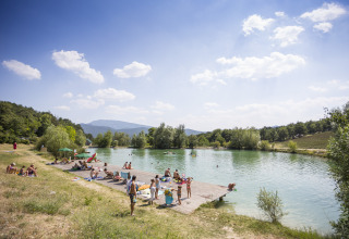 Des personnes se détendent près d'un lac au Village Huttopia Dieulefit – Glamping Drôme-Provence par beau temps.