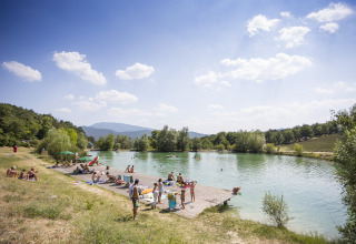 Mensen genieten aan het meer bij Village Huttopia Dieulefit – Glamping Drôme-Provence op een zonnige dag.