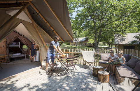 Famille se détendant sur la terrasse de leur tente glamping au Village Huttopia Dieulefit, Drôme-Provence.
