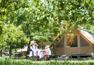 Family eats outdoors at picnic table by luxury tent in Village Huttopia Dieulefit, Drôme-Provence glampsite.