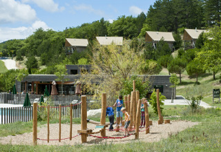 Bambini giocano su un parco giochi in legno presso Village Huttopia Dieulefit – Glamping Drôme-Provence immerso nel verde.