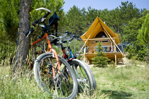 Deux vélos appuyés contre un arbre devant une tente lodge à Village Huttopia Dieulefit, en pleine nature provençale.