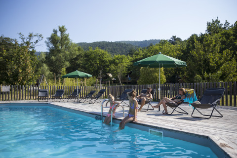 Des vacanciers se détendent près de la piscine au Village Huttopia Dieulefit – Glamping Drôme-Provence, entourés de verdure.