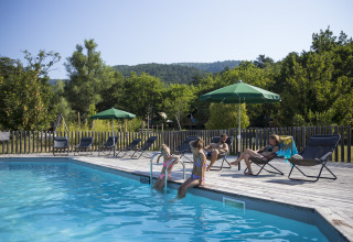 Gasten ontspannen bij het zwembad van Village Huttopia Dieulefit – Glamping Drôme-Provence, omgeven door natuur.