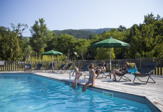 Gasten ontspannen bij het zwembad van Village Huttopia Dieulefit – Glamping Drôme-Provence, omgeven door natuur.