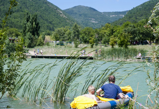 Deux personnes dans un bateau gonflable sur un lac à Village Huttopia Dieulefit, entouré de nature et de montagnes.