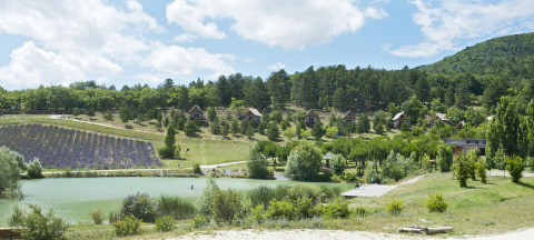 Scenic view of Village Huttopia Dieulefit Glamping Drôme-Provence with pond, cabins, lavender and woods.