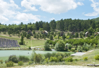 Vista su Village Huttopia Dieulefit Glamping Drôme-Provence con lago, capanne, lavanda e bosco.