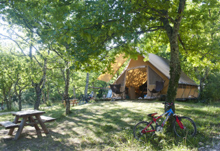 Glamping presso Village Huttopia Dieulefit – Glamping Drôme-Provence con tenda, biciclette e tavolo da picnic in foresta.