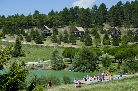 Glamping Village Huttopia Dieulefit in Drôme-Provence met hutten en bezoekers ontspannen aan het meer.