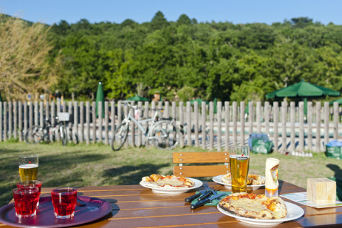 Tavolo da picnic con pizze e bevande all’aperto, biciclette sullo sfondo a Village Huttopia Dieulefit Glamping.