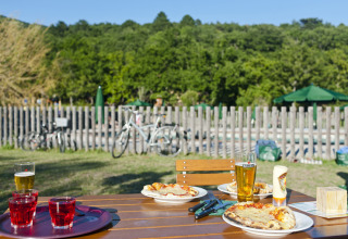 Buitentafel met pizza’s en drankjes, fietsen op de achtergrond bij Village Huttopia Dieulefit Glamping.