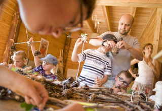 Children and adults making crafts with pinecones and sticks in a wooden hut at Village Huttopia Dieulefit.