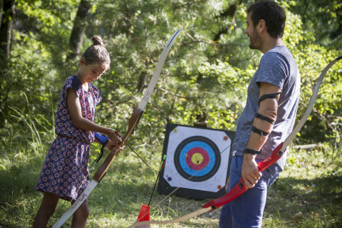 Padre e figlia che praticano tiro con l'arco nella natura a Village Huttopia Dieulefit – Glamping Drôme-Provence.