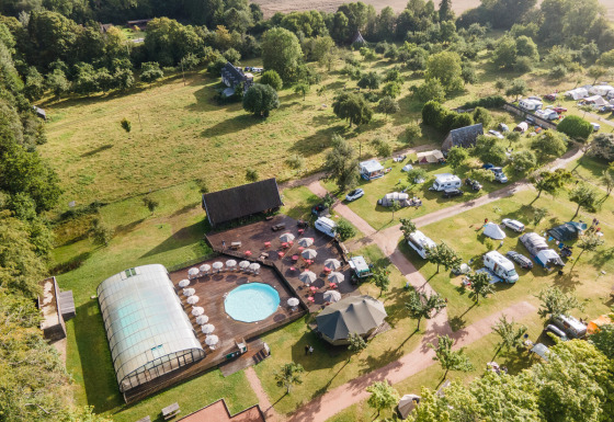 Vista aérea de Huttopia Calvados-Normandie, glamping con piscina, tiendas, caravanas y mucho verde alrededor.