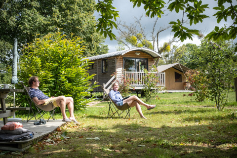 Twee mensen ontspannen bij hun glampingaccommodatie op Huttopia Calvados-Normandië, omgeven door natuur.