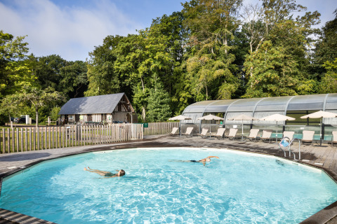Piscine extérieure au Huttopia Calvados-Normandie, entourée de chaises longues et de nature verdoyante.