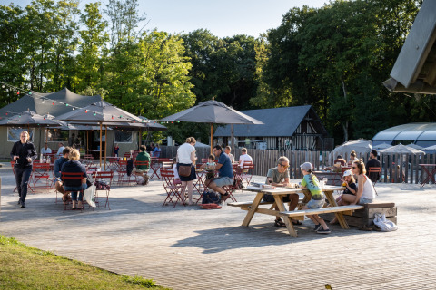 Außenbereich von Huttopia Calvados-Normandie Glamping mit Gästen, Sonnenschirmen und grüner Umgebung.