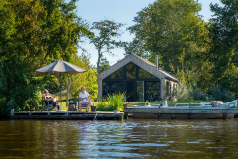 Zwei Personen entspannen auf einem Steg bei Pean Buiten - Natuurhuisjes Friesland im Grünen am Wasser.