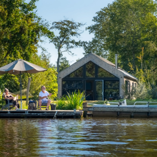 Two people relaxing on a dock by Pean Buiten - Natuurhuisjes Friesland, surrounded by water and greenery.